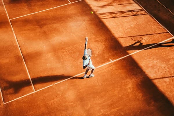 Joueur de tennis au service sur une terre battue, vu du dessus